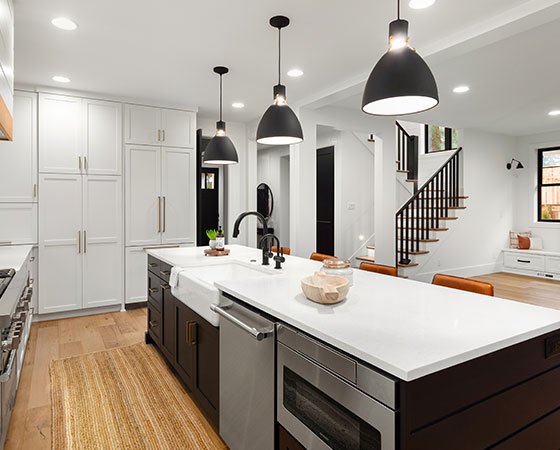 First-floor open-space kitchen featuring a kitchen island with a white countertop and black cabinets. The wooden floor adds warmth and contrast to the contemporary design. White cabinets in the background complete the sleek and stylish aesthetic, creating a modern culinary space.
