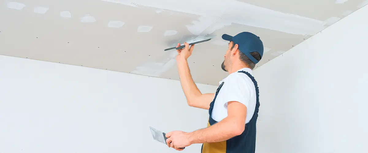 Worker performing drywall repair in Downey, patching ceiling with spackle.