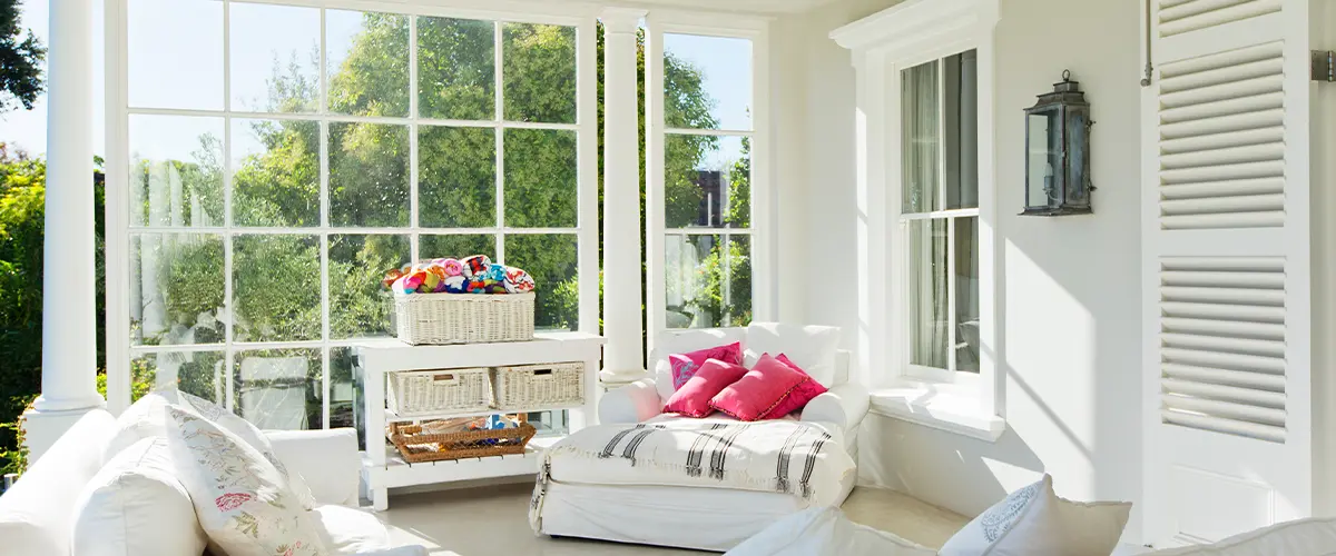 Bright attached Adu sunroom with large windows, white furniture, colorful throw pillows, and a cozy, inviting atmosphere perfect for relaxation.