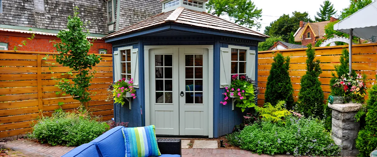 Charming ADU with blue exterior, white doors, flower boxes, surrounded by lush greenery