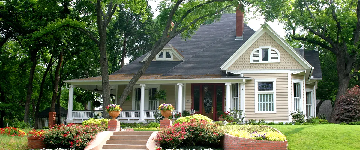 Charming vintage house in Cerritos with lush garden and large front porch surrounded by green trees and blooming flowers.