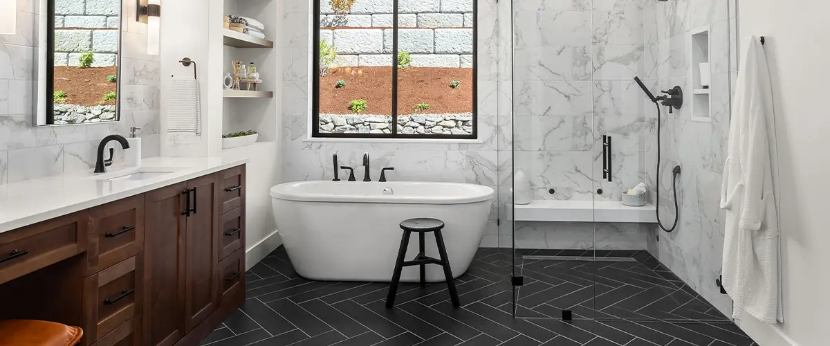 Modern bathroom featuring a freestanding tub, marble walls, and herringbone-pattern black tile flooring, perfect for a sleek design.