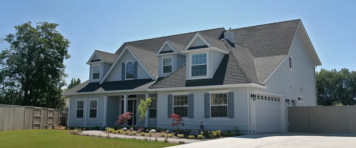 Modern gray home with large windows, landscaped front yard, and clean driveway under blue sky.