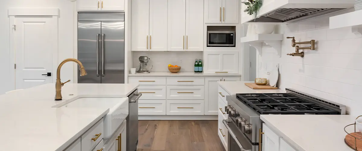 Modern white kitchen with gold accents, stainless steel appliances, and a large center island with pendant lighting.