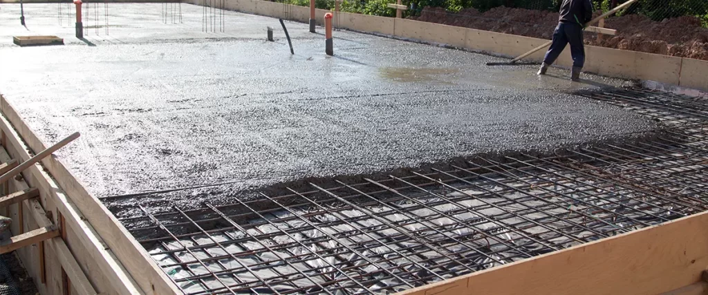 Contractor smoothing freshly poured concrete foundation with steel reinforcement for structural support.