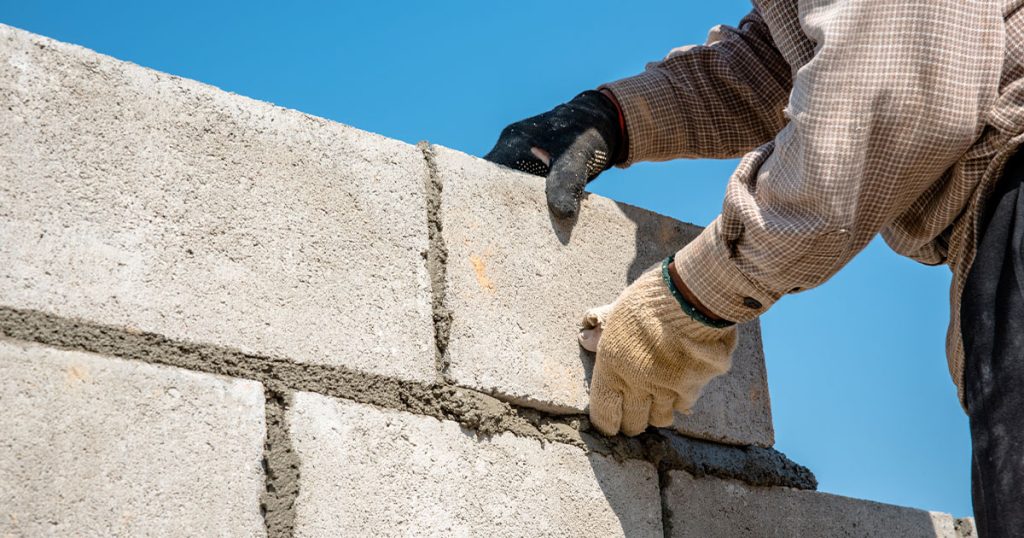 Worker laying concrete blocks with mortar to build a durable wall for construction projects.