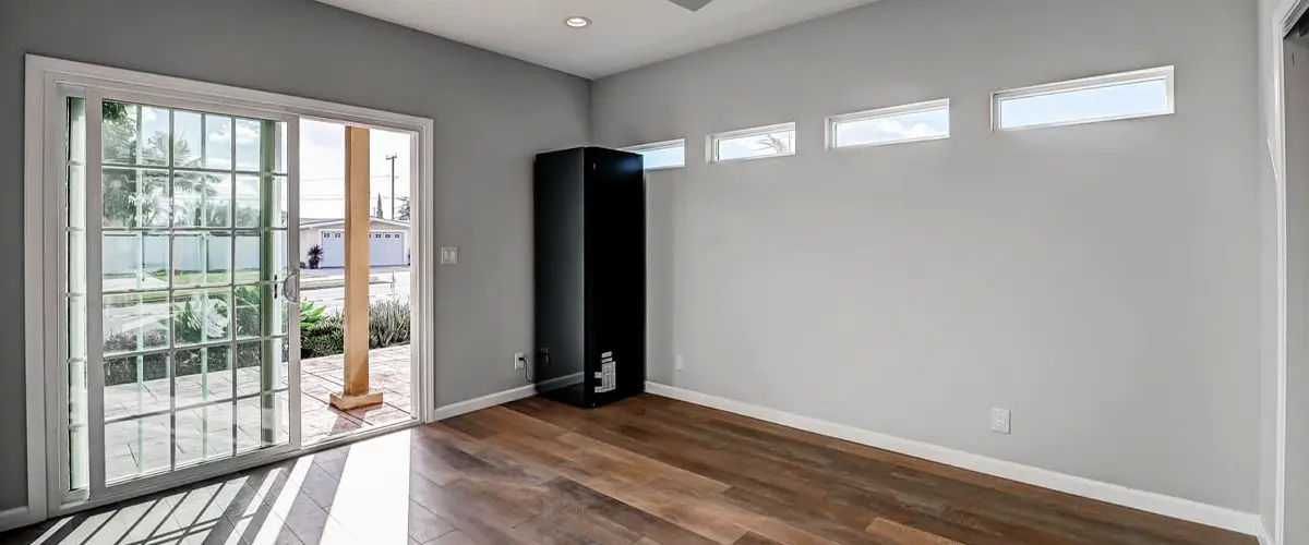 Empty modern room with wood floors, ceiling fan, sliding glass door, and clerestory windows letting in natural light.