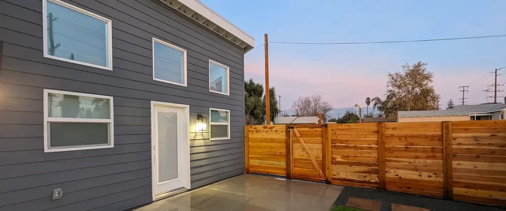 Modern backyard with gray siding, concrete patio, and horizontal wood privacy fence at sunset.