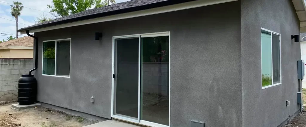 Newly built ADU with gray stucco exterior, sliding glass door, and rainwater barrel in a California backyard
