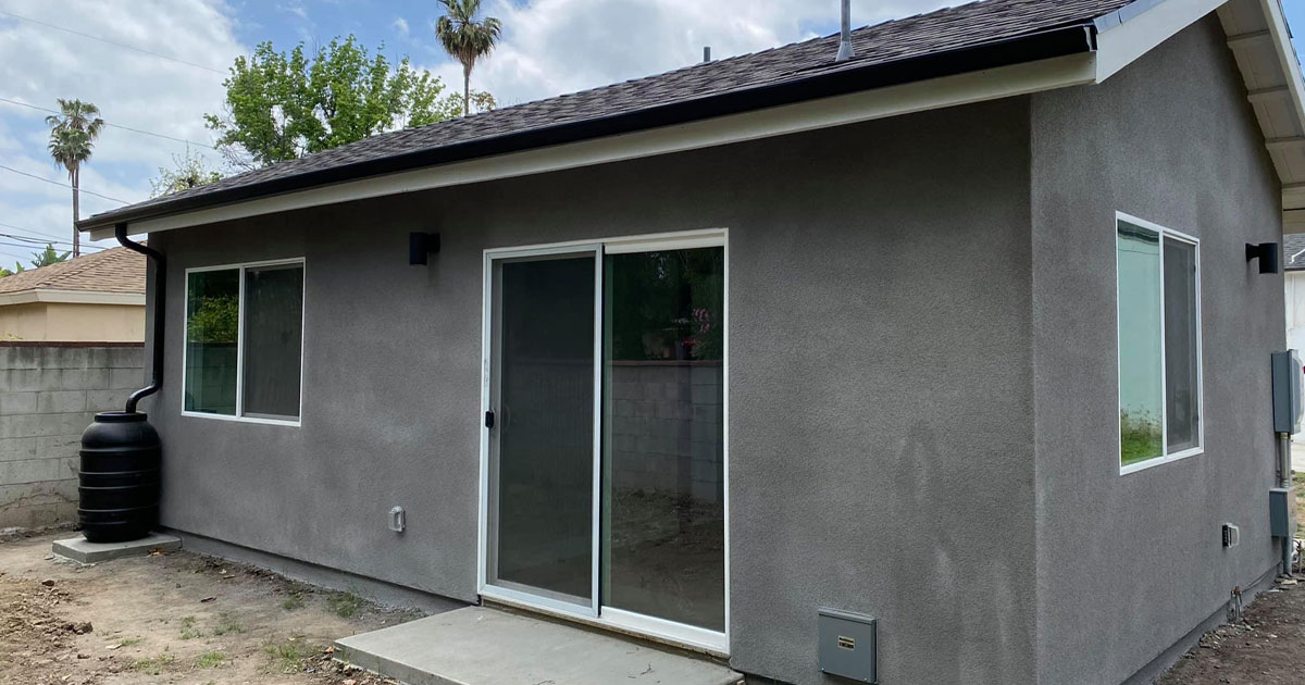Newly built ADU with gray stucco exterior, sliding glass door, and rainwater barrel in a California backyard