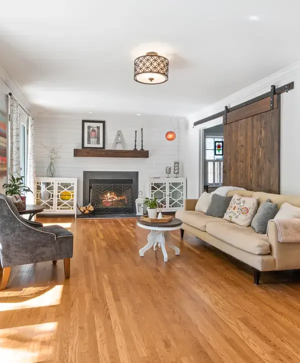 A bright living room with wood flooring, shiplap wall, a traditional fireplace, and a large rustic sliding barn door, showcasing stylish interior home improvements in Whittier, CA.