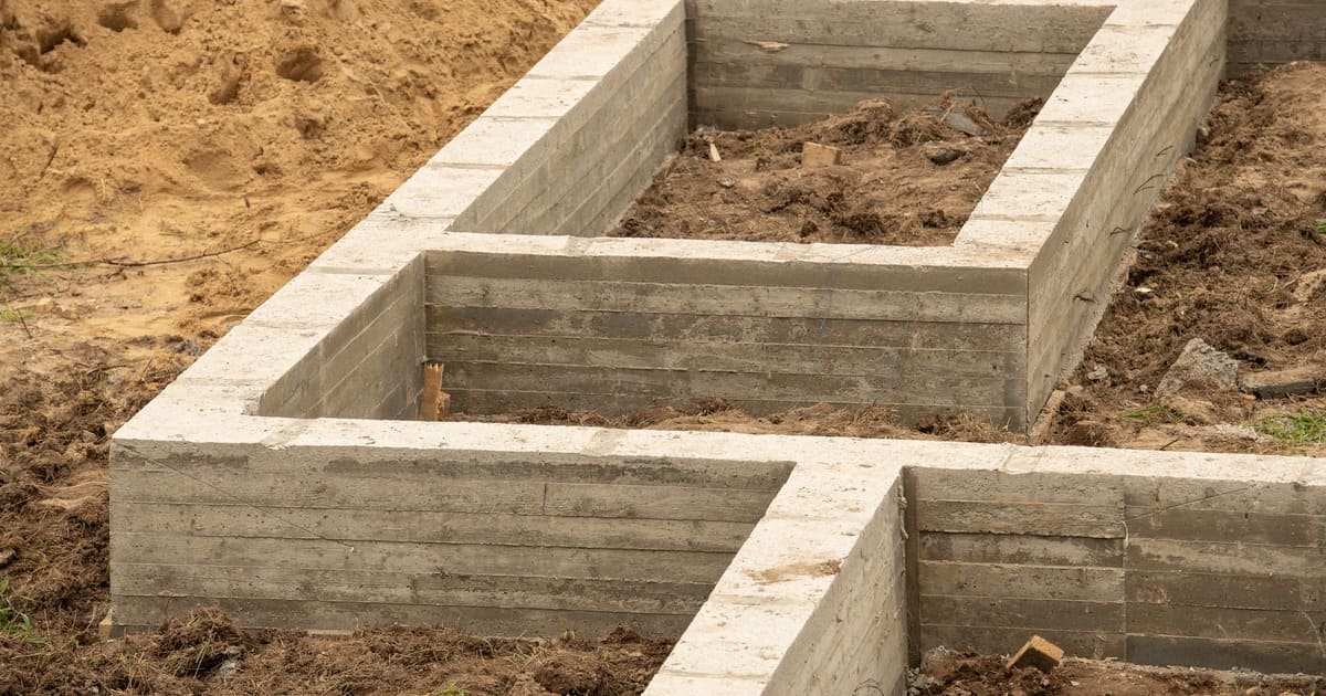 A newly poured concrete perimeter foundation showing the structural footings and wall layout on a residential construction site.