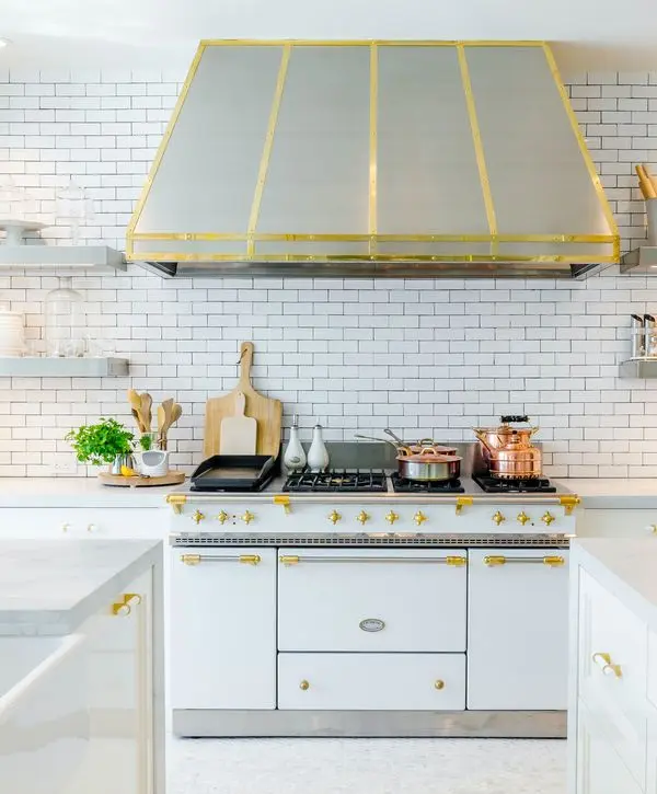 High-end kitchen remodeling in Norwalk, CA showcasing a white professional-grade gas range with gold hardware and a matching oversized vent hood against white subway tile.