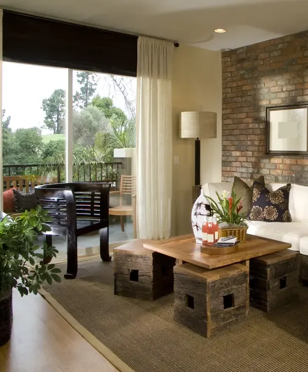 A cozy living space with a natural brick accent wall, unique wooden coffee table, and balcony view, highlighting expert home improvements in Pico Rivera, CA.