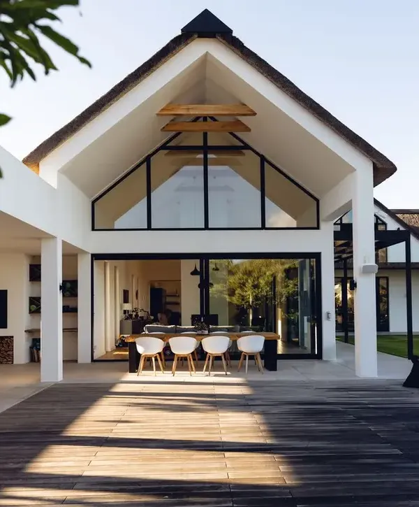 High-end modern home featuring a large vaulted glass gable, white exterior walls, and a spacious wooden deck with outdoor dining furniture, designed by a premier home builder in Rancho Palos Verdes, CA.