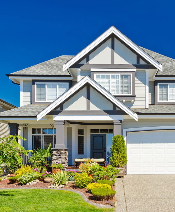 A two-story modern craftsman home in Rowland Heights, CA, featuring light gray siding, a stone-base porch, and a beautifully landscaped front garden with colorful flowers.
