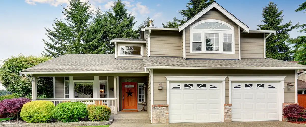 A large modern home with olive gray siding, a prominent two-car garage with white doors, and a decorative red front door featuring a black star.