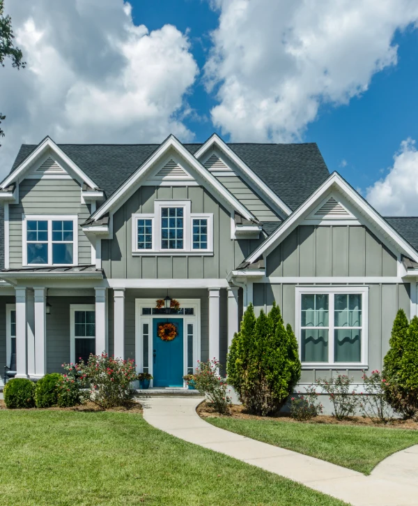 A beautiful grey house with multiple gables, white trim, and a bright blue front door, showcasing the craftsmanship of a custom home builder in Garden Grove, CA.
